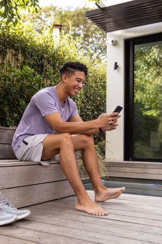 Asian Man Relaxing with Smartphone Outdoors on Modern Patio
