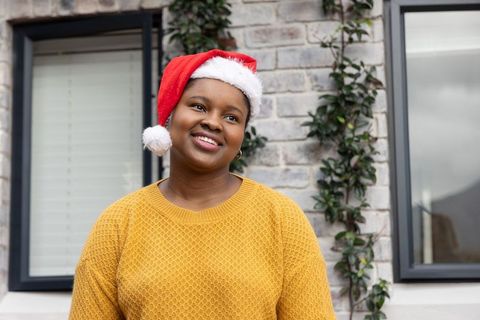 African american woman wearing santa hat and mustard sweater smiling outdoors