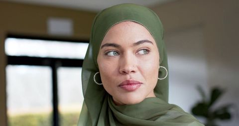 Indian woman wearing olive hijab gazing out window with hoop earrings and nose stud