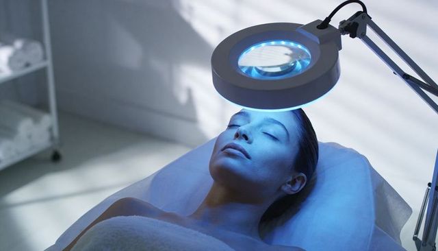 Woman receiving blue led light therapy facial on spa bed, clinical skincare treatment