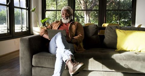 Senior Man Relaxing on Sofa Reading Tablet in Sunlit Living Room