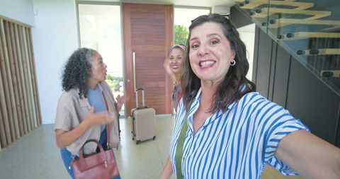 Hispanic friends taking selfie in bright modern home entry with luggage and handbags