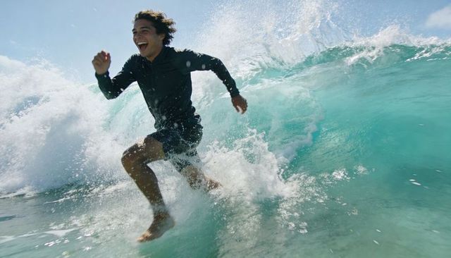 Young man running through turquoise breaking surf laughing in bright sun on tropical beach