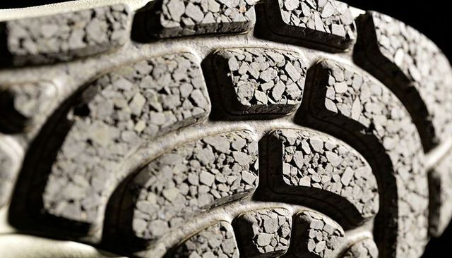 Worn sneaker sole revealing embedded gravel, cracked lugs and rugged tread texture