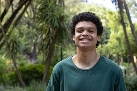 Smiling african american young man wearing green tee standing in sunlit urban park