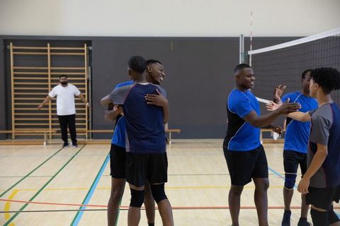 African american volleyball team hugging and high-fiving celebrating victory in indoor gym
