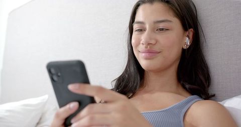 Teen Girl Relaxing in Bed with Smartphone and Earphones