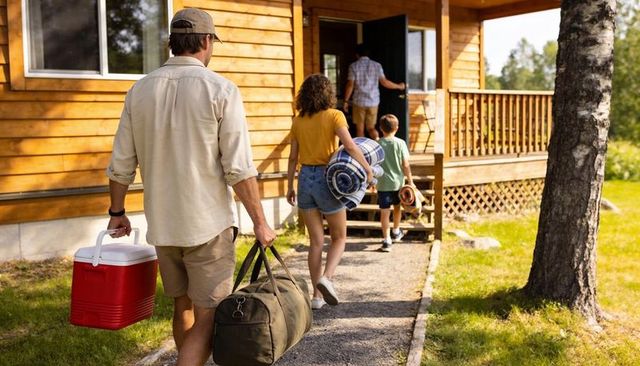 Family walking to cabin carrying cooler and luggage for summer lake vacation getaway