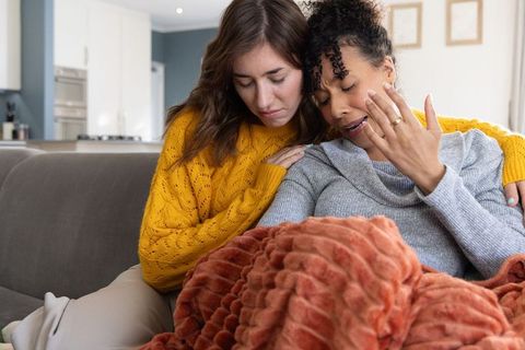 Multiracial female partners comforting tearful woman on couch showing emotional support