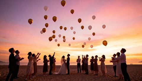 Sunset Beach Wedding Celebration with Guests Releasing Gold and White Balloons