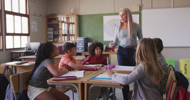Classroom scene with diverse students interacting with female teacher, perfect for educational content, multicultural learning environments, back to school promotions, and materials highlighting elementary education