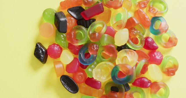 Assorted colorful gummy candies in various shapes placed against a yellow backdrop. Ideal for use in advertisements for candies, confectionery shops, children's parties, or sugar-themed content. Perfect visual for blogs or articles about snacks, sweet treats, or food photography.