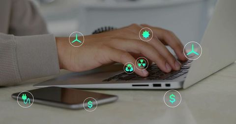 Typing hands on laptop with renewable energy, sustainability and finance icons and smartphone