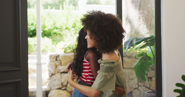 Happy biracial mother and daughter embracing in sunny living room. Domestic life, motherhood, family and togetherness.
