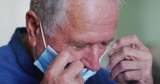 Elderly man wearing and adjusting medical face mask, focusing on healthcare and safety measures. Useful for topics related to COVID-19, health precautions, protection against virus, elderly care, or hygiene practices.