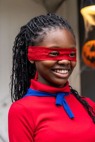 Smiling african american girl wearing red superhero eye mask and blue scarf on halloween