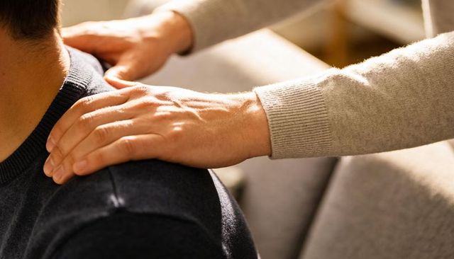 Hands giving gentle shoulder massage on seated partner in cozy golden light