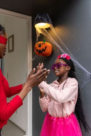African american mother and daughter celebrating halloween on porch clapping hands