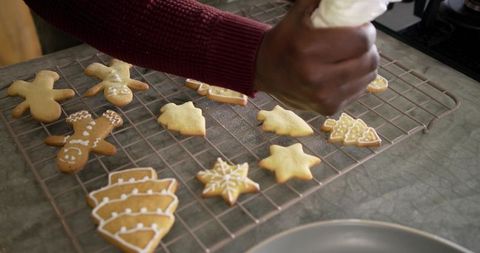 African American man decorating gingerbread cookies with white icing on cooling rack