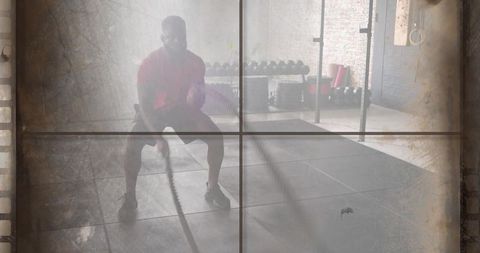 Fit man swinging battle ropes in industrial gym for strength and cardio conditioning