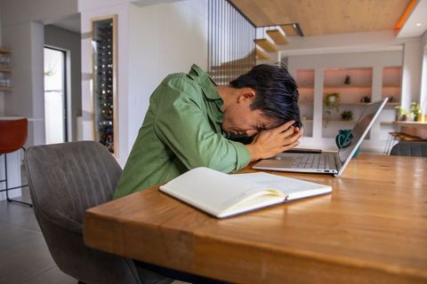 Overwhelmed asian man leaning on laptop, covering face, remote work burnout at home