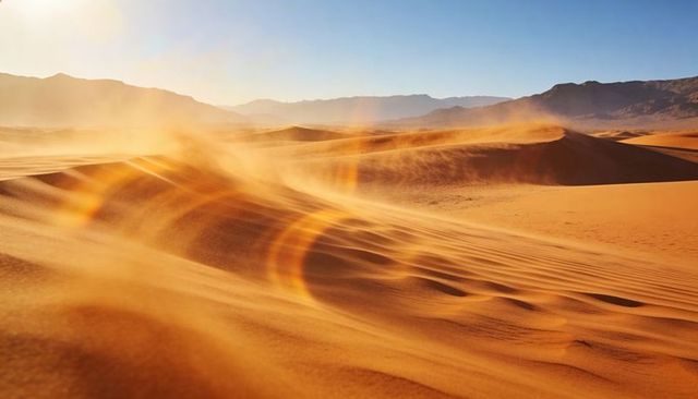 Golden wind-sculpted sand dunes shifting across desert basin with glowing lens flare