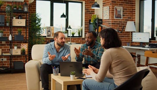 Collaborating team brainstorming in casual modern lounge with laptop and exposed brick wall