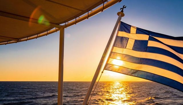 Greek flag fluttering from ship mast during golden sunset over calm aegean sea horizon
