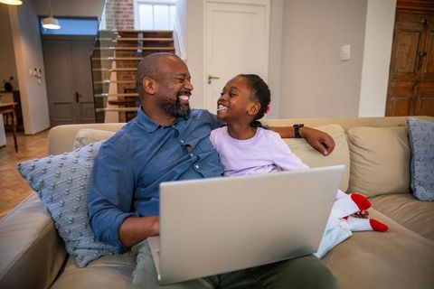 African american father laughing with daughter on couch using laptop for bonding