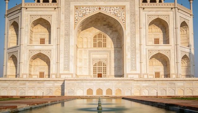 Sunlit taj mahal facade with central iwan and reflecting pool showing perfect symmetry