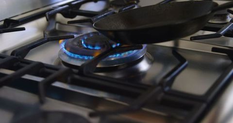 Hand Holding Black Cast Iron Pan Over Lit Gas Stove - Download Free Stock Images Pikwizard.com
