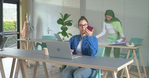 Diverse female team collaborating in sunny coworking space with woman in hijab using laptop