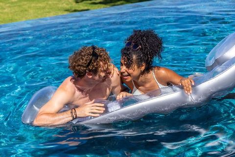 Laughing couple lounging on silver pool float, playful summer backyard romance