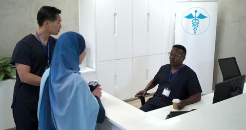 Multicultural medical team chatting at reception desk holding coffee cups in modern clinic