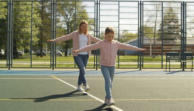 Caregiver and child balancing on court line wearing matching pink hoodies and jeans