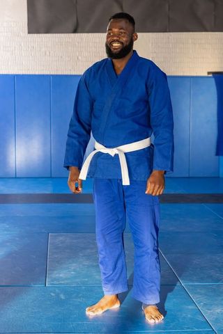 Smiling Martial Artist Wearing Blue Gi Stands Confidently on Mats