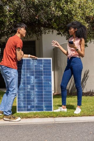 Young diverse coworkers discussing home solar panel installation on suburban front lawn