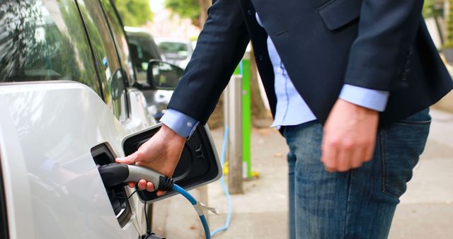 A middle-aged Caucasian businessman is charging an electric vehicle, with copy space. His focus on sustainable transportation reflects a growing trend towards eco-friendly practices in business travel.