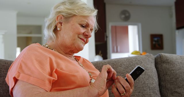 Senior Caucasian woman checks her phone at home, with copy space. She appears engaged and content in a comfortable living room setting.
