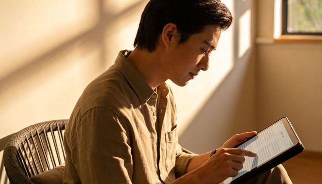 Man reading tablet by sunlit window in minimalist home interior, warm natural light