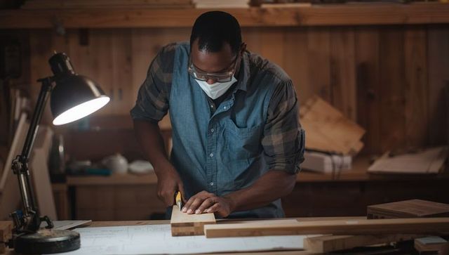 Protective woodworker sawing in workshop