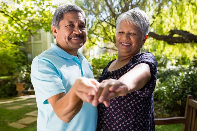 Senior couple enjoying a dance in a lush garden on a sunny day. Perfect for use in advertisements promoting active lifestyles for seniors, retirement communities, or healthcare services. Ideal for illustrating themes of love, happiness, and togetherness in older age.