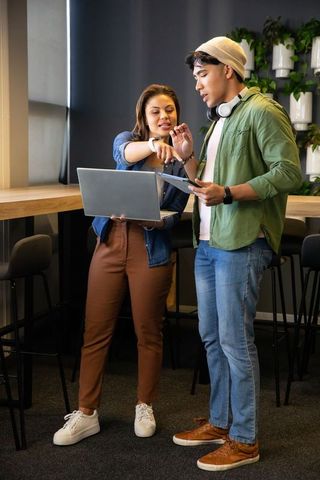 Diverse coworkers collaborating over laptop and tablet in modern coworking lounge
