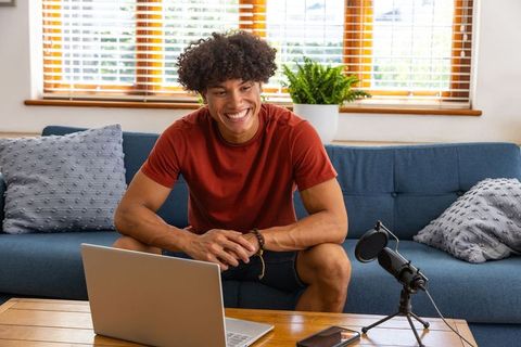 Smiling Young Man Podcasting at Home with Laptop and Microphone