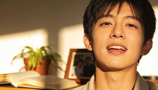 Sunlit asian student speaking and smiling at desk with open book and indoor plant, golden hour portr