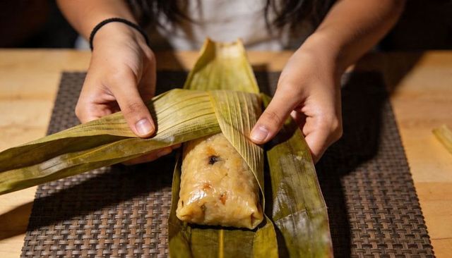 Hands unwrapping banana leaf glutinous rice dumpling zongzi revealing sticky rice filling