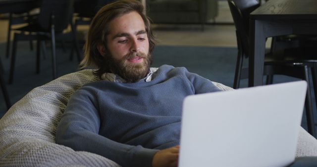 Young Man Relaxing on Bean Bag Working on Laptop in Modern Office - Download Free Stock Images Pikwizard.com