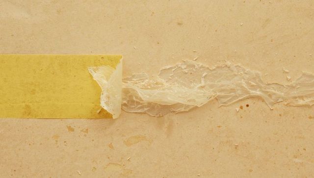 Peeling yellow masking tape leaving translucent adhesive film across textured paper