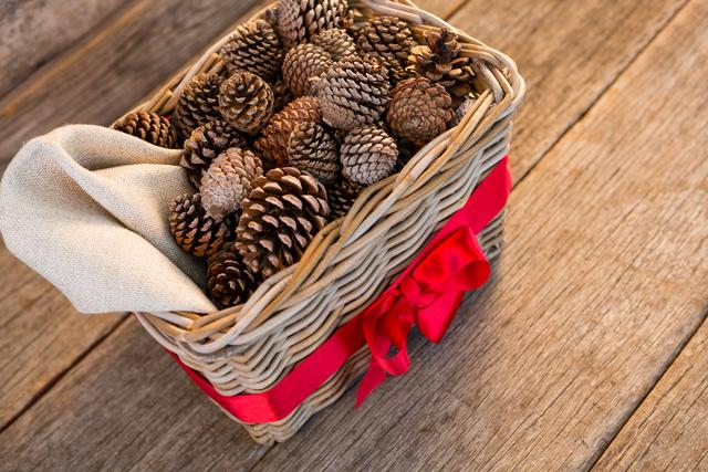 Pine cones in wicker basket tied with red ribbon on wooden plank during christmas time