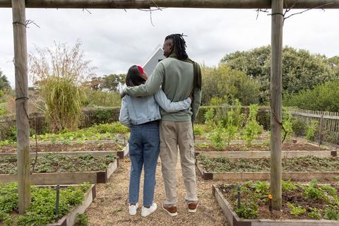 Diverse couple embracing under pergola in community garden with raised vegetable beds